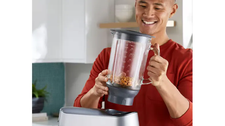 A person lifting a blender jug filled with peanuts A person lifting a blender jug filled with peanuts