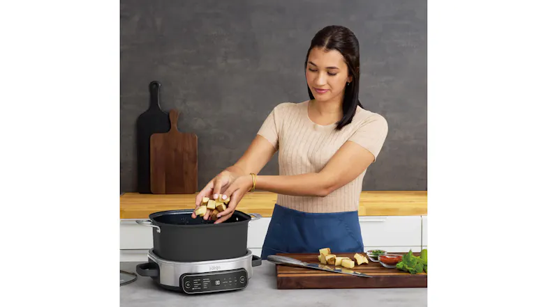A woman adding chopped potatoes into the Ninja PossibleCooker Pro on a kitchen counter A woman adding chopped potatoes into the Ninja PossibleCooker Pro on a kitchen counter