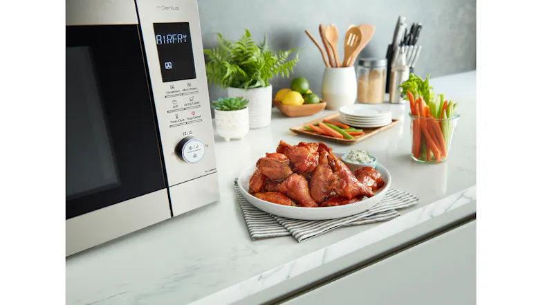 A cooked chicken wing served on a plate beside the microwave on a kitchen counter A cooked chicken wing served on a plate beside the microwave on a kitchen counter