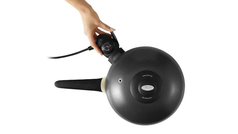 A hand is adjusting the temperature dial on a black electric skillet with a long handle A hand is adjusting the temperature dial on a black electric skillet with a long handle