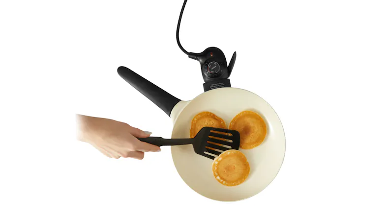 A hand flipping small pancakes in a white electric skillet using a black spatula A hand flipping small pancakes in a white electric skillet using a black spatula