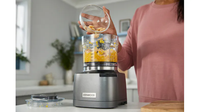 A person pouring chickpeas into the clear Kenwood chopper bowl for food prep A person pouring chickpeas into the clear Kenwood chopper bowl for food prep