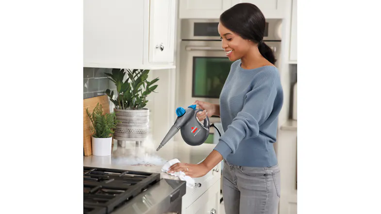 A person uses the Bissell Steam Shot to steam‑clean a kitchen countertop near a stovetop A person uses the Bissell Steam Shot to steam‑clean a kitchen countertop near a stovetop