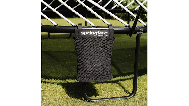Black mesh storage pocket hanging from the frame of a Springfree trampoline outdoors over green grass Black mesh storage pocket hanging from the frame of a Springfree trampoline outdoors over green grass