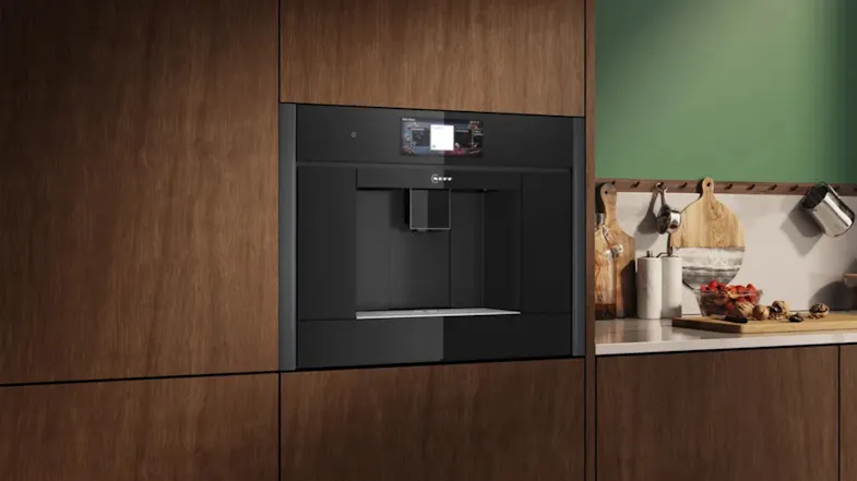 An automatic coffee machine fitted into wood cabinetry next to a kitchen counter with boards, jars, and accessories An automatic coffee machine fitted into wood cabinetry next to a kitchen counter with boards, jars, and accessories
