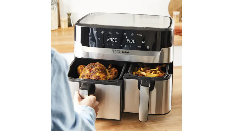 A hand pulling out dual air fryer baskets containing a cooked chicken and fries on a kitchen counter A hand pulling out dual air fryer baskets containing a cooked chicken and fries on a kitchen counter