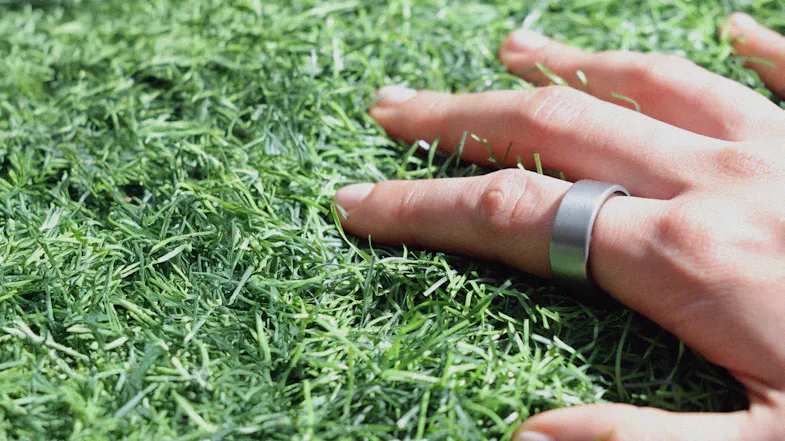 A hand wearing a smart ring on green artificial grass A hand wearing a smart ring on green artificial grass