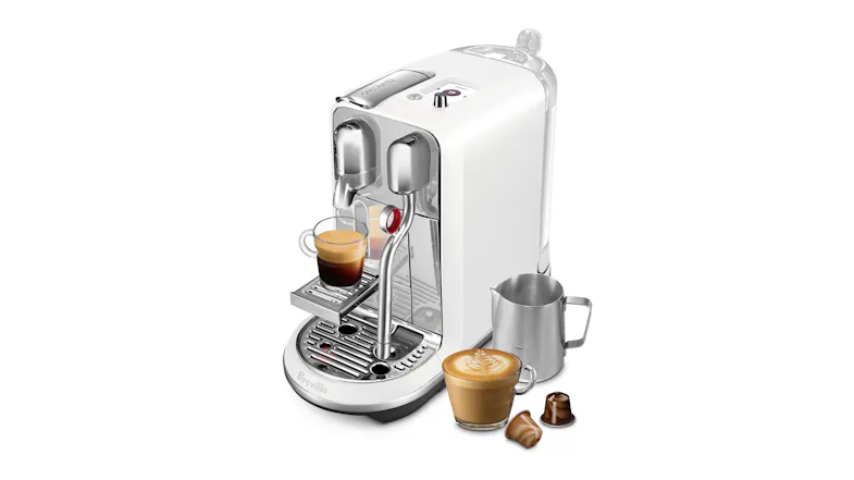 Right view of a coffee machine with 2 cups of coffee, a stainless pitcher and two brown capsules Right view of a coffee machine with 2 cups of coffee, a stainless pitcher and two brown capsules
