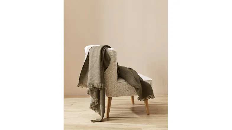 A light-coloured chair with wooden legs is draped with an olive throw blanket A light-coloured chair with wooden legs is draped with an olive throw blanket