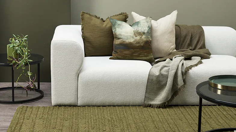 A close-up of a white sofa with green and white cushions and an olive throw blanket A close-up of a white sofa with green and white cushions and an olive throw blanket