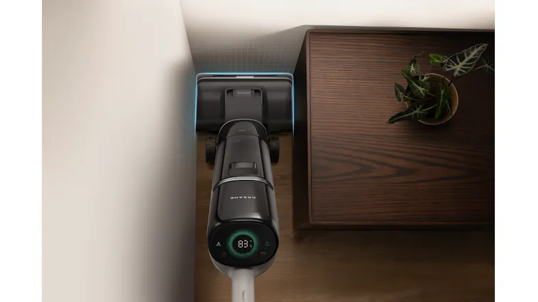 The vacuum cleaner being used to clean out dust and dirt on a tight corner beside a sidetable The vacuum cleaner being used to clean out dust and dirt on a tight corner beside a sidetable