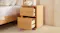 A narrow bedside table next to a bed with open drawers. A narrow bedside table next to a bed with open drawers.
