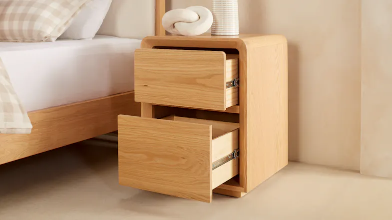 A narrow bedside table next to a bed with open drawers. A narrow bedside table next to a bed with open drawers.