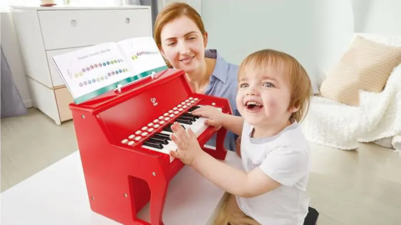 An adult and a child playing the red toy piano. An adult and a child playing the red toy piano.