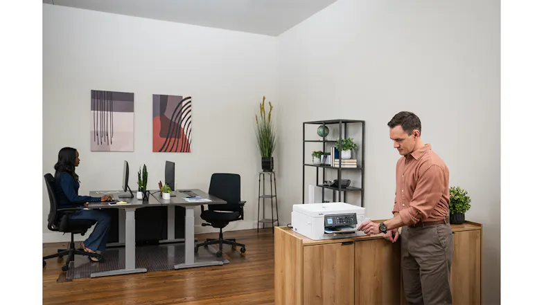 A view of a man retrieving a printed document from the sleek, grey Brother printer. A view of a man retrieving a printed document from the sleek, grey Brother printer.