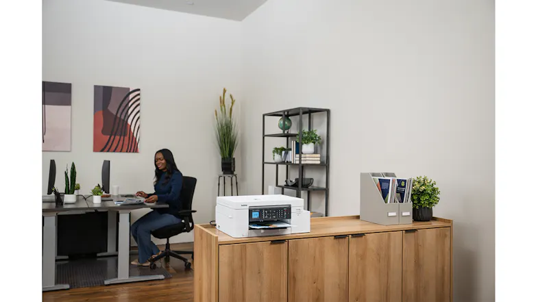 A view of the unit with a printed document in its output tray on a cabinet in an office. A view of the unit with a printed document in its output tray on a cabinet in an office.