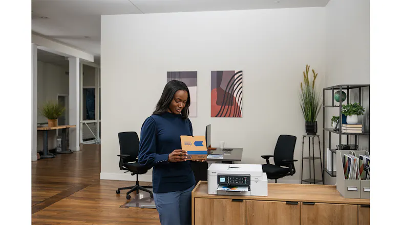 A view of a woman holding a product box while standing next to the Brother All-in-One Inkjet Printer. A view of a woman holding a product box while standing next to the Brother All-in-One Inkjet Printer.