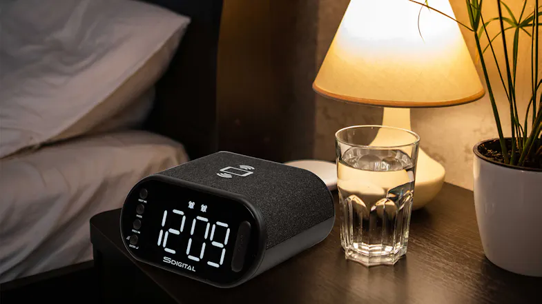 A digital alarm clock on a bedside table in a cozy, nighttime setting. A digital alarm clock on a bedside table in a cozy, nighttime setting.
