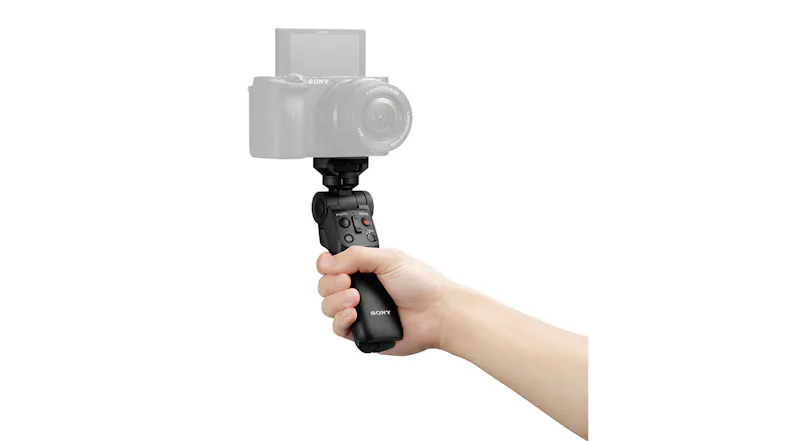Hand holding black camera grip with integrated control buttons and a reference camera Hand holding black camera grip with integrated control buttons and a reference camera
