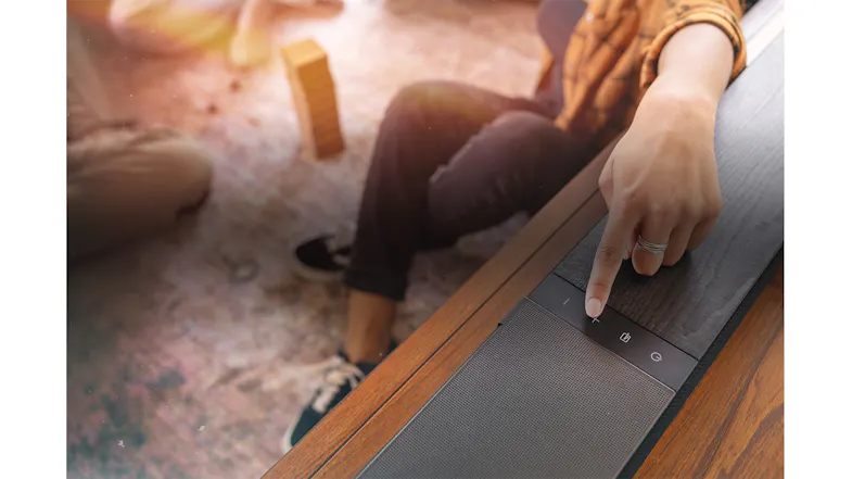 Top view of the soundbar, with a woman pressing the volume control Top view of the soundbar, with a woman pressing the volume control