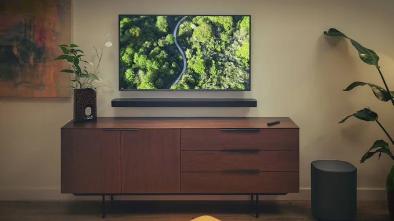 A living room with a wooden cabinet, a wall-mounted soundbar, and a floor speake A living room with a wooden cabinet, a wall-mounted soundbar, and a floor speake
