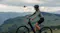 Cyclist riding uphill in hilly terrain, followed by a drone Cyclist riding uphill in hilly terrain, followed by a drone