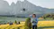 Person holding a remote control operates a hovering drone with mountains and green fields behind Person holding a remote control operates a hovering drone with mountains and green fields behind