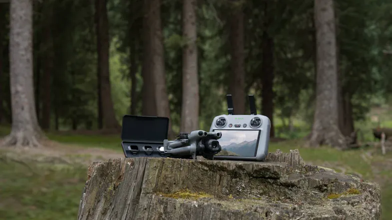 Folded DJI Mini 5 Pro drone and open carrying bag with accessories on a tree stump in a wooded area Folded DJI Mini 5 Pro drone and open carrying bag with accessories on a tree stump in a wooded area