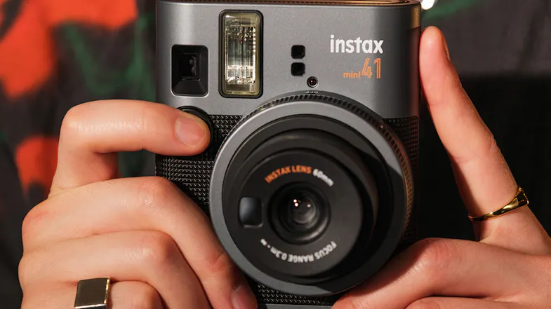 A person holding a black retro camera with rings and a patterned shirt A person holding a black retro camera with rings and a patterned shirt