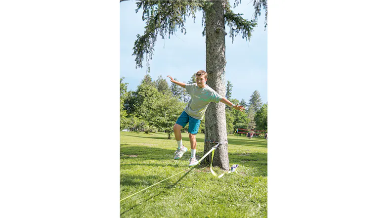 A person mid-air balancing on a slackline in a sunny park A person mid-air balancing on a slackline in a sunny park