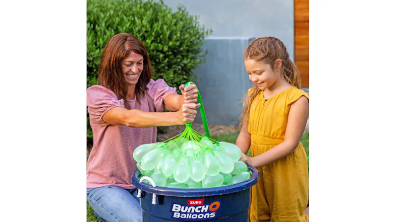Two people filling green water balloons in a bucket outdoors Two people filling green water balloons in a bucket outdoors