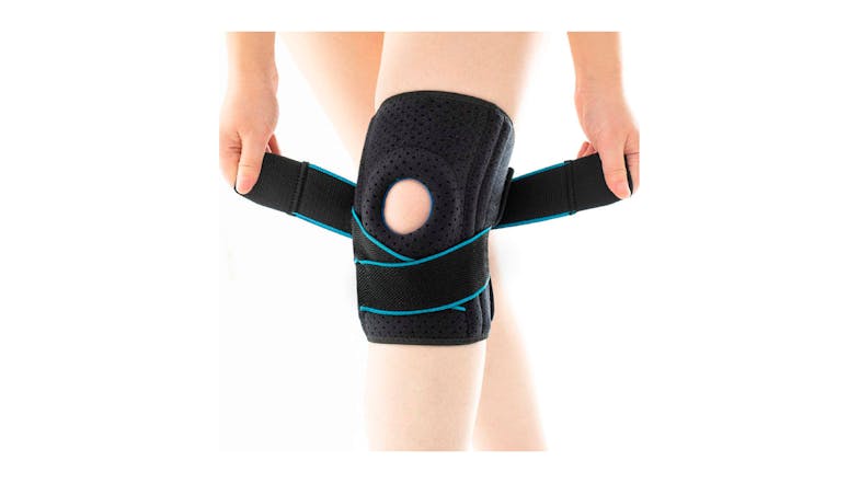 A person’s hand fastening an adjustable knee brace with an open patella design A person’s hand fastening an adjustable knee brace with an open patella design