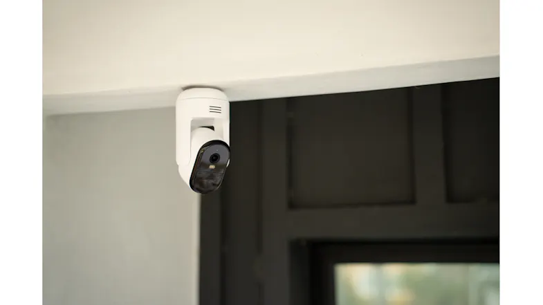 A white camera mounted near the ceiling corner with a window A white camera mounted near the ceiling corner with a window