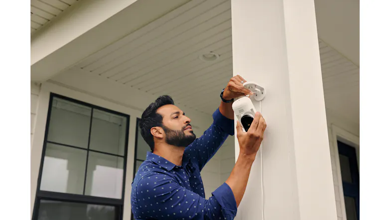 A person installing a security camera on a white column A person installing a security camera on a white column