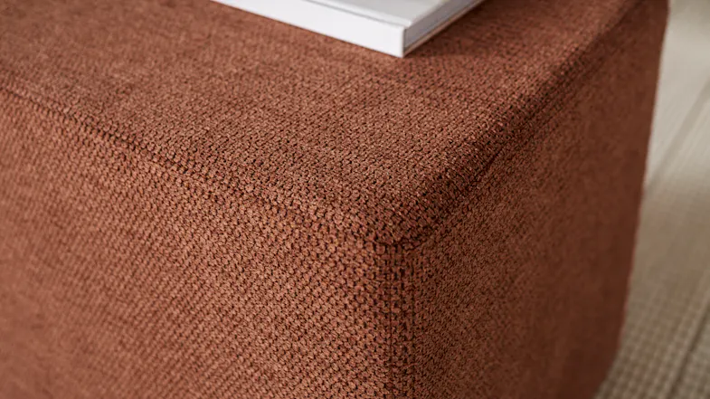 Close up of Polar Square Footstool in terracotta fabric with a simple cube shape and smooth, upholstered finish Close up of Polar Square Footstool in terracotta fabric with a simple cube shape and smooth, upholstered finish