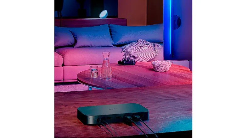 Philips HDMI Sync Box on a wooden table in a living room with colourful ambient lighting from Hue lights Philips HDMI Sync Box on a wooden table in a living room with colourful ambient lighting from Hue lights