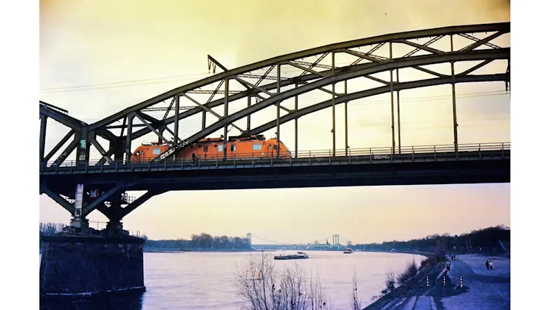 A photo of an orange train crossing a steel bridge over a river A photo of an orange train crossing a steel bridge over a river