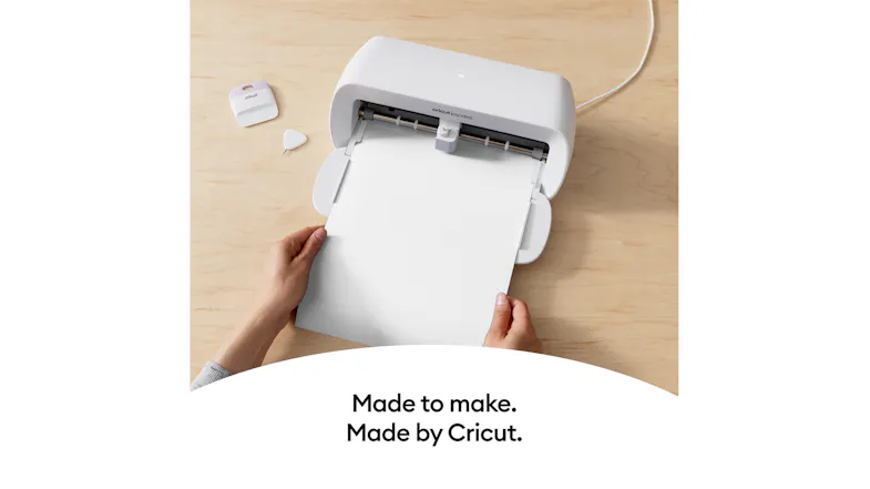 Hands loading a white sheet into the Cricut cutter on a wood surface Hands loading a white sheet into the Cricut cutter on a wood surface