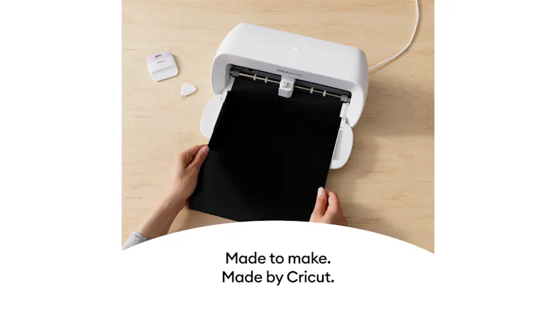 Hands loading a black sheet into the Cricut cutter on a wood surface Hands loading a black sheet into the Cricut cutter on a wood surface