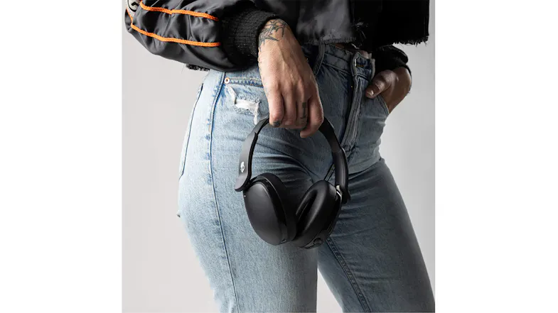 Person in jeans and a striped jacket holding black headphones Person in jeans and a striped jacket holding black headphones