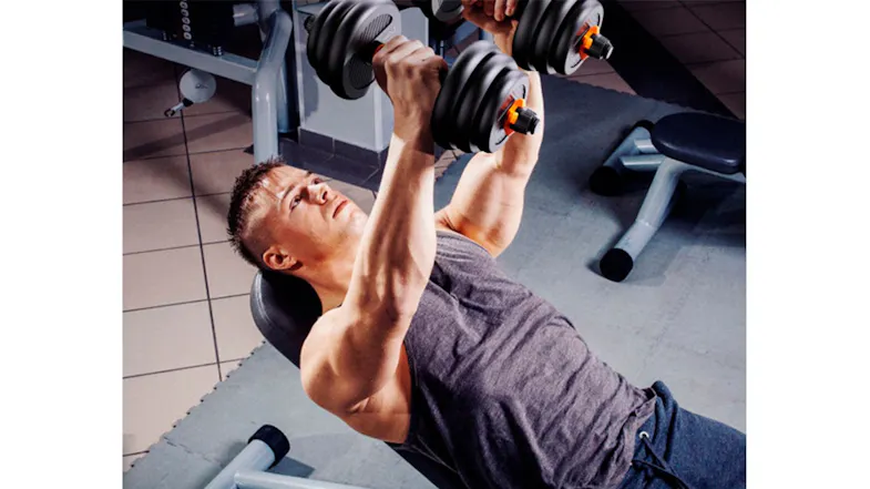Man lifting adjustable dumbbells while lying on an incline bench in a gym setting Man lifting adjustable dumbbells while lying on an incline bench in a gym setting
