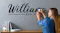 Person applying “Williams EST. 201” wall decal above a wooden surface Person applying “Williams EST. 201” wall decal above a wooden surface