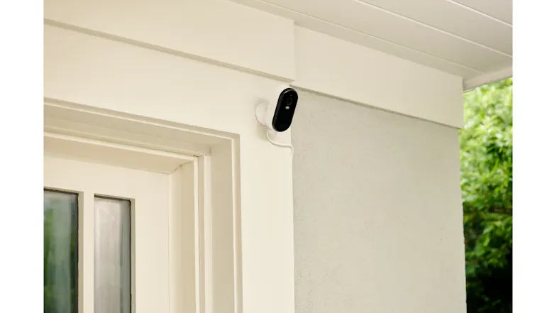 Wired security camera above the door with a white bracket and greenery Wired security camera above the door with a white bracket and greenery