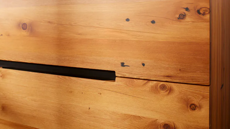 Detail shot of the drawer front with dark wood knots and the sleek, recessed black metal handle Detail shot of the drawer front with dark wood knots and the sleek, recessed black metal handle