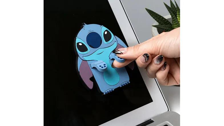 Hand attaching Disney Stitch screen cleaner to a laptop screen near a small plant Hand attaching Disney Stitch screen cleaner to a laptop screen near a small plant