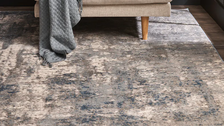 Close-up of the Frankie Rug beneath an armchair, emphasising its textured surface and tonal variations Close-up of the Frankie Rug beneath an armchair, emphasising its textured surface and tonal variations