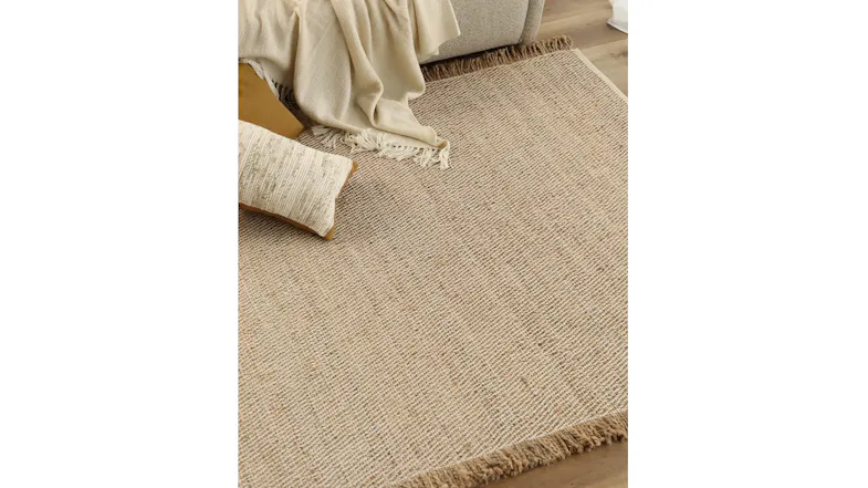 Lifestyle image of a rug in a cosy setting placed under a sofa with a cream throw and textured cushions Lifestyle image of a rug in a cosy setting placed under a sofa with a cream throw and textured cushions