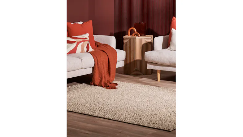 Modern living room featuring the Miranda Rug in pebble under two light beige sofas with rust-coloured cushions and throw Modern living room featuring the Miranda Rug in pebble under two light beige sofas with rust-coloured cushions and throw