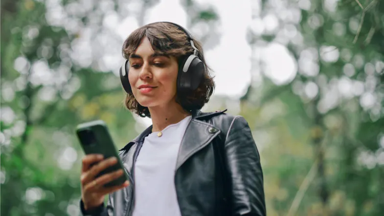 Person holding a smartphone while wearing Sennheiser HDB 630 headphones outdoors Person holding a smartphone while wearing Sennheiser HDB 630 headphones outdoors