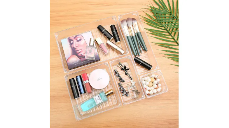 A clear organiser trays on a wooden surface holding makeup items, brushes, lipsticks, perfume, and accessories A clear organiser trays on a wooden surface holding makeup items, brushes, lipsticks, perfume, and accessories